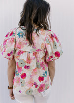 Back view of Model wearing a cream top with watercolor floral and short bubble sleeves.