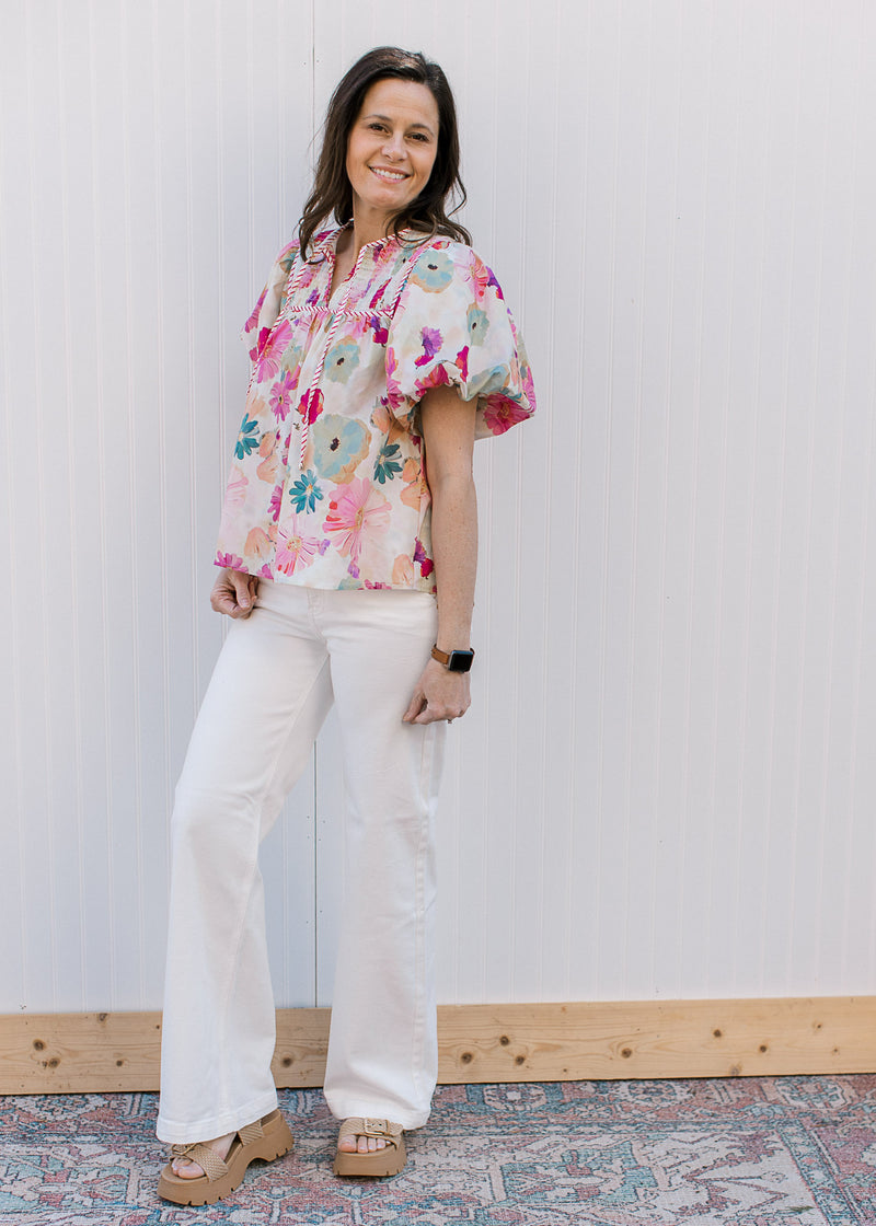 Model wearing white pants and a cream top with watercolor floral and short bubble sleeves.