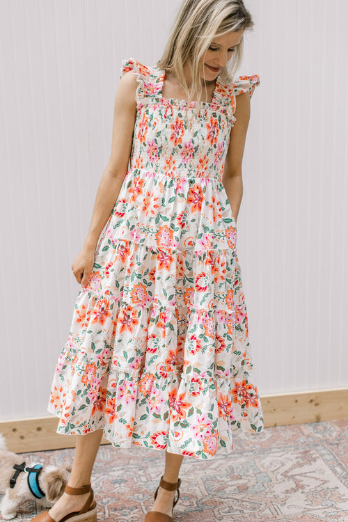 Model wearing a cream midi with bright floral, smocked bodice and ruffle sleeves. 