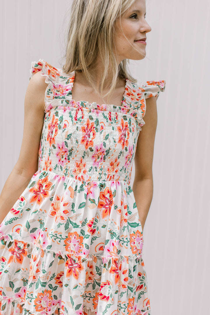Close up of smocked bodice, square neck and ruffle sleeves on a cream midi with bright floral. 