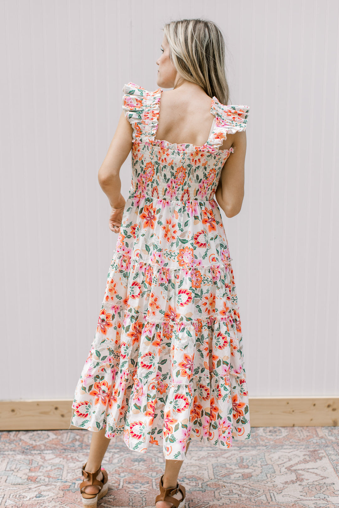 Back view of Model wearing a cream midi with bright floral, smocked bodice and ruffle sleeves.