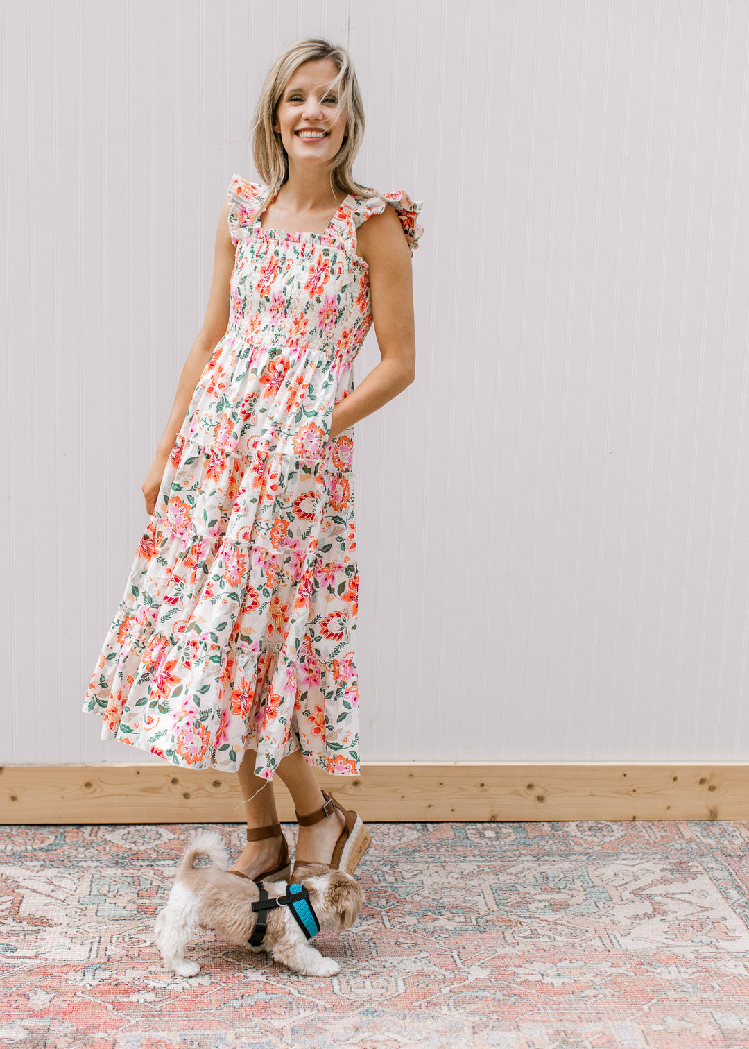 Model wearing heels with a cream midi with bright floral, smocked bodice and ruffle sleeves.