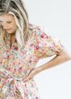 Close up view of short puff sleeves and tie at waist on a cream dress with a colored floral pattern.