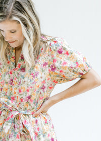 Close up view of short puff sleeves and tie at waist on a cream dress with a colored floral pattern.