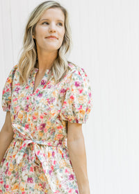 Model wearing a cream v-neck dress with a mixed colored floral pattern and a tie at the waist. 