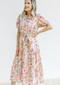 Model wearing a cream v-neck dress with a mixed colored floral pattern and short puff sleeves. 