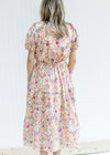 Back view of Model wearing a cream v-neck dress with a colored floral pattern and short sleeves. 