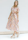 Model wearing heals with a cream v-neck dress with a colored floral pattern and short sleeves. 