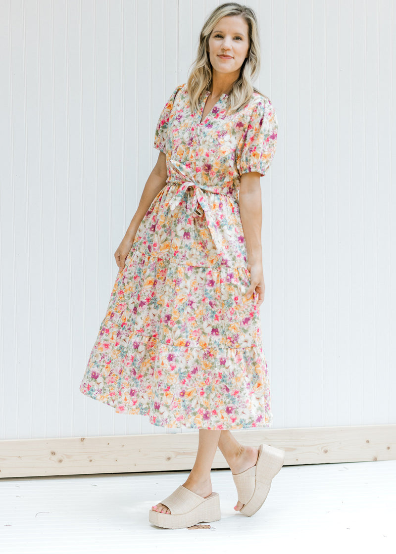 Model wearing heals with a cream v-neck dress with a colored floral pattern and short sleeves. 