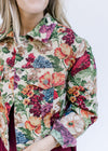 Close up view of tapestry jacket with a cream background and red, blue and green hued floral. 