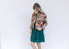 Model wearing a long sleeve floral tapestry jacket with a button closure and a crop fit.