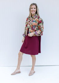 Model wearing mules and a red dress with a long sleeve floral tapestry jacket with a crop fit.