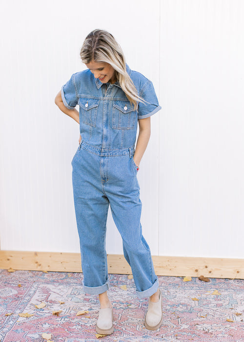 Model wearing a medium washed denim jumpsuit with a hidden zipper, wide legs and short sleeves. 