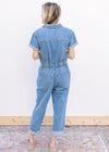 Back view of model wearing a medium washed, short sleeve denim jumpsuit with an elastic waist.
