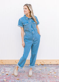 Model wearing mules and a medium washed denim jumpsuit with wide legs and short sleeves. 