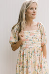 Close up of pleated bust, square neck and short sleeves on a yellow and pink floral dress.