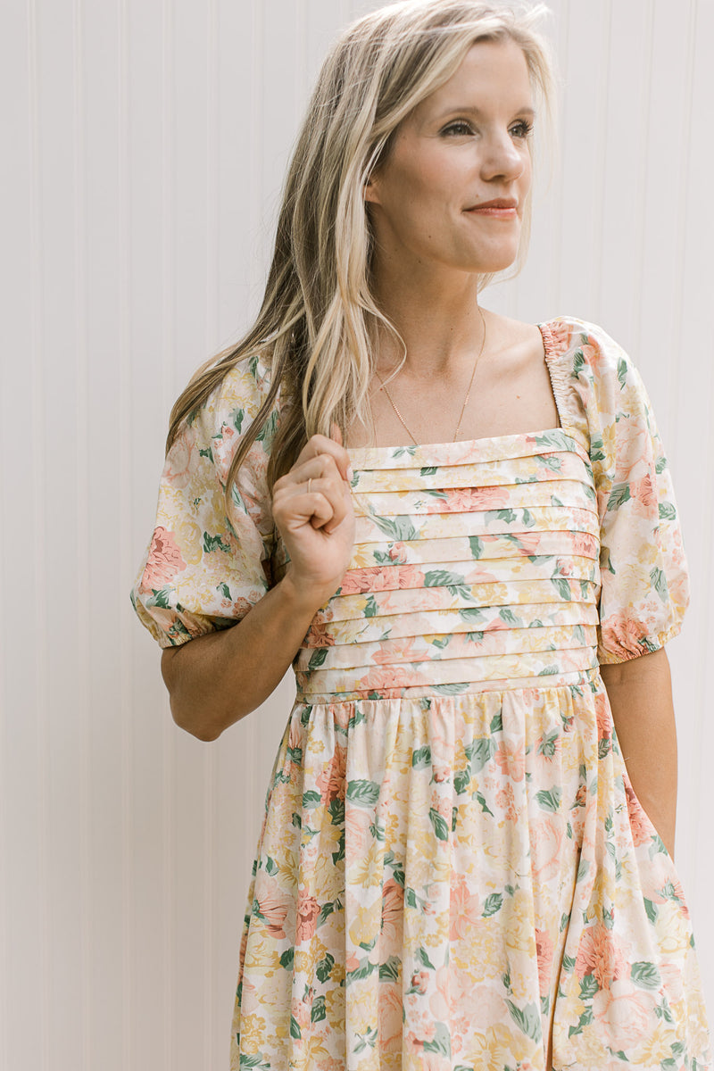 Close up of pleated bust, square neck and short sleeves on a yellow and pink floral dress.