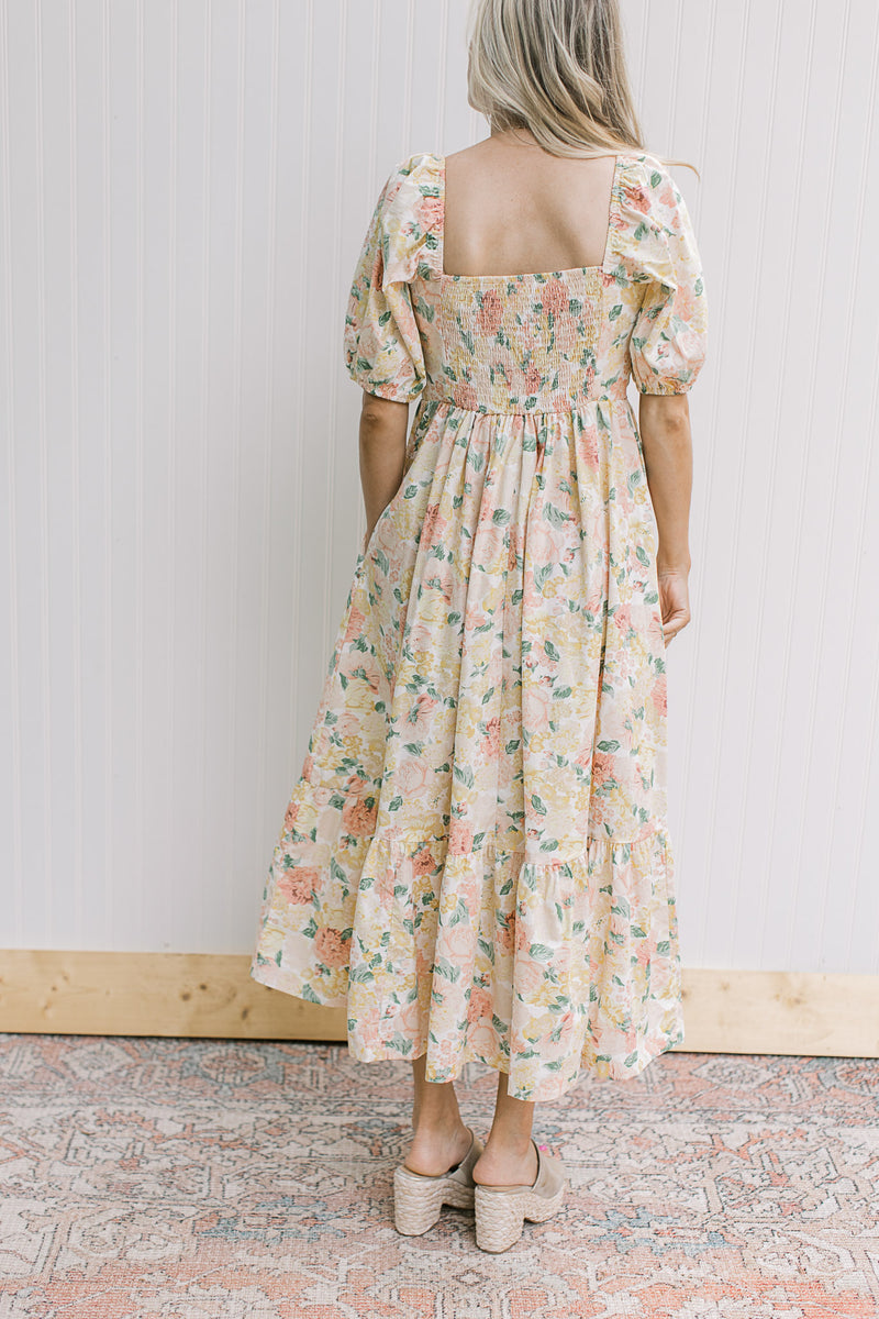 Back view of model wearing a yellow and pink floral dress with a smocked back and square neck.