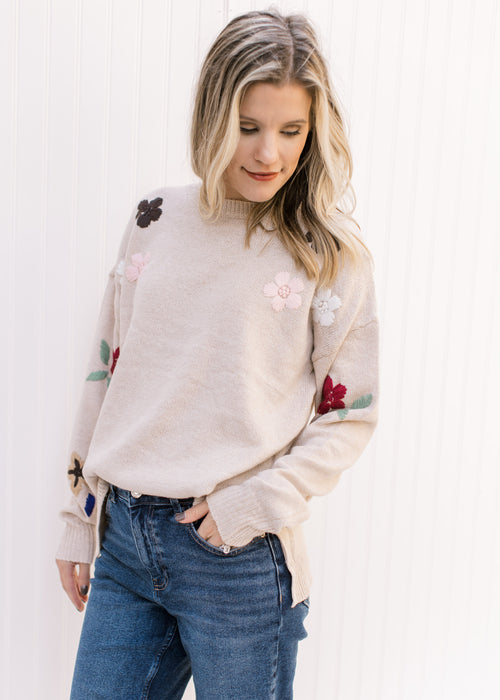 Model wearing a taupe sweater with embroidered floral detail on long sleeves and a round neck.