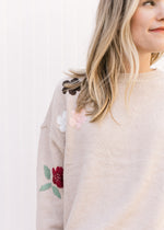 Close up view of embroidered floral detail on long sleeves of a taupe sweater with split sides. 