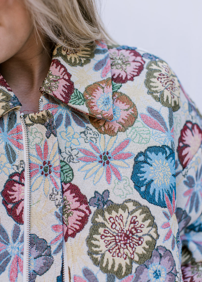 Close up of embroidered flowers and collar on a cream zip-up jacket with long sleeves. 