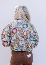 Back view of Model wearing a cream jacket with embroidered flowers and long sleeves. 