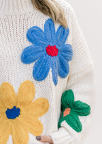 Close up of flowers on a cream knit top with an oversized fit, long sleeves and a mock neckline