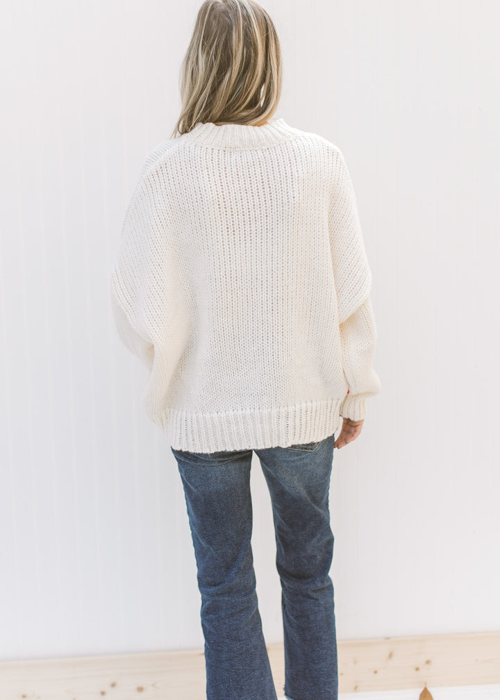 Back view of Model wearing a cream oversized sweater with red, yellow, blue, pink and red flowers.