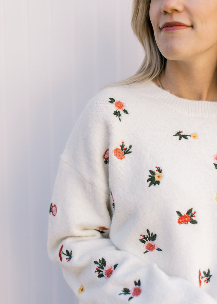Close up of embroidered yellow and orange flowers on a cream sweater with long sleeves. 