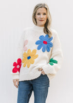 Model wearing a cream oversized knit sweater with red, yellow, blue, pink and red flowers.