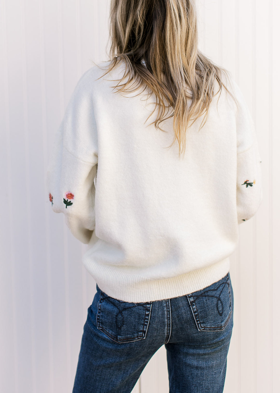 Back view of Model wearing a cream sweater with pink and yellow flowers and long sleeves. 