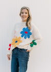Model wearing a cream knit sweater with red, yellow, blue, pink and red flowers and long sleeves. 