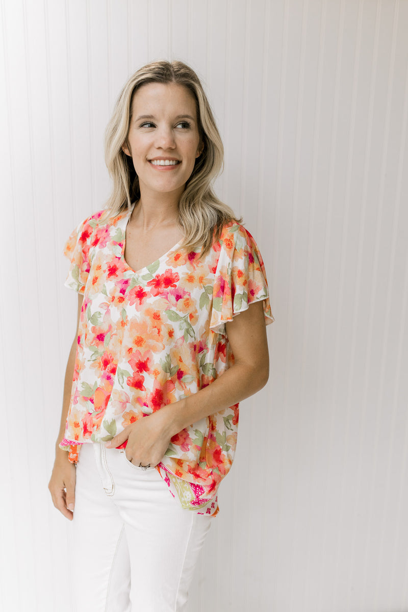 Model wearing a white top with red, orange and green floral print, short sleeves and a border print.
