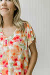 Close up of red, orange and green floral pattern on a white top with a v-neck and short sleeves. 