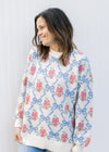 Model wearing a cream top with blue bows and pink flowers, long sleeves and round neck.