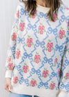 Close up of  blue bows and pink flowers on a cream sweater with long sleeves and a round neck.