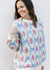 Model wearing a cozy cream top with blue bows and pink flowers, long sleeves and round neck.