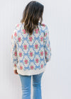 Back view of Model wearing a cream top with blue bows and pink flowers and long sleeves.