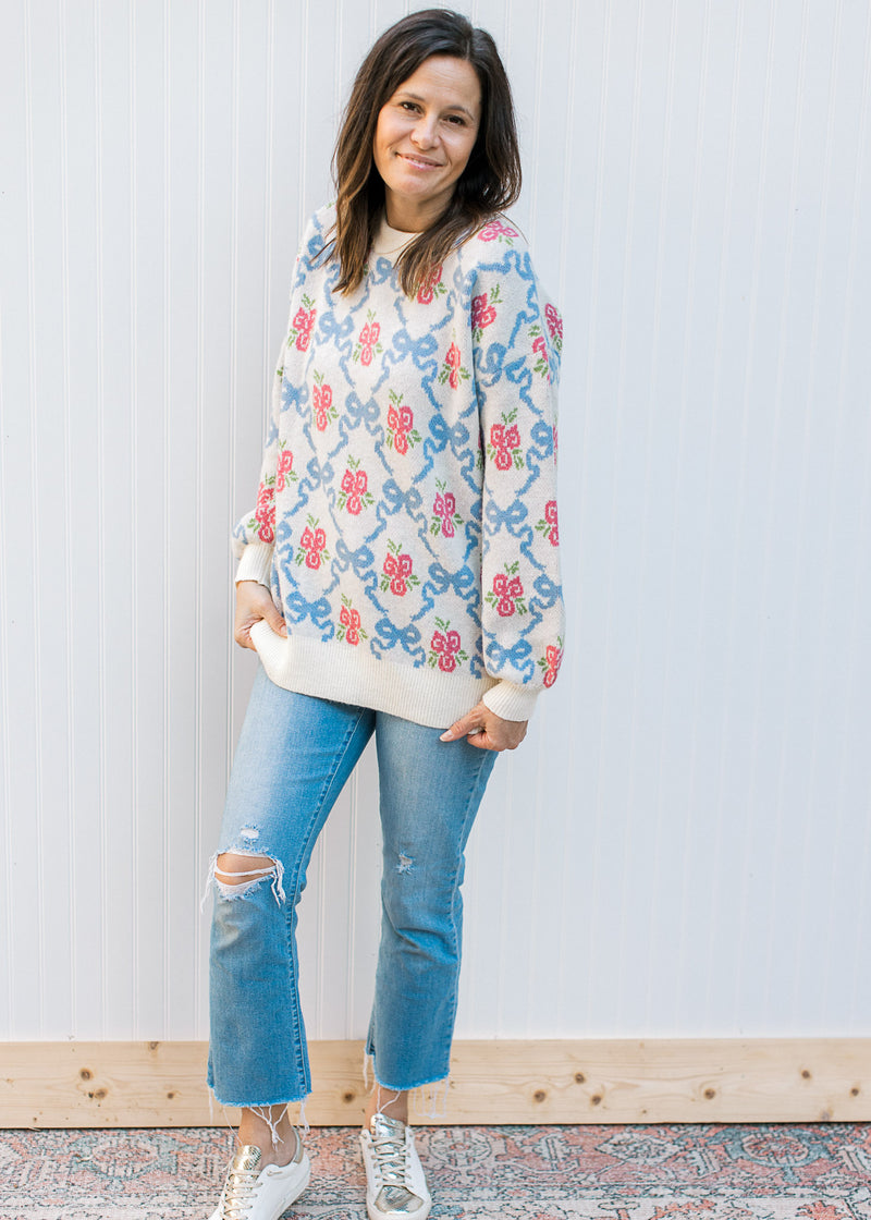 Model wearing jeans, sneakers and a cream top with blue bows and pink flowers.