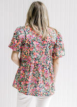 Back view of Model wearing a bright floral top with a black background and bubble short sleeves.