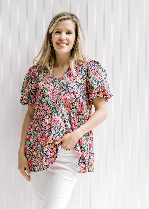 Model wearing a bright floral babydoll top with a black background and bubble short sleeves. 
