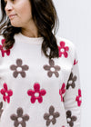 Close up of brown and maroon flowers on an ivory long sleeve sweater with a round neck. 