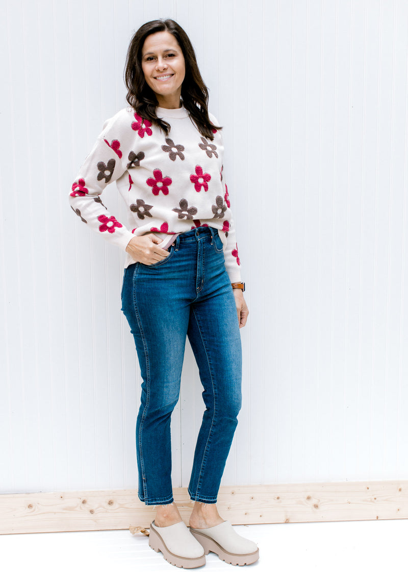 Model wearing jeans and mules with an ivory long sleeve sweater with maroon and brown flowers.  