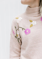 Close up of mock neck and embroidered flowers on a blush sweater with long sleeves. 