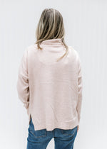 Back view of Model wearing a blush sweater with embroidered flowers and a mock neck.
