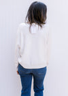 Back view of Model wearing a white sweater with colorful embroidered flowers and long sleeves. 
