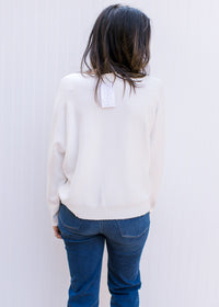 Back view of Model wearing a white sweater with colorful embroidered flowers and long sleeves. 