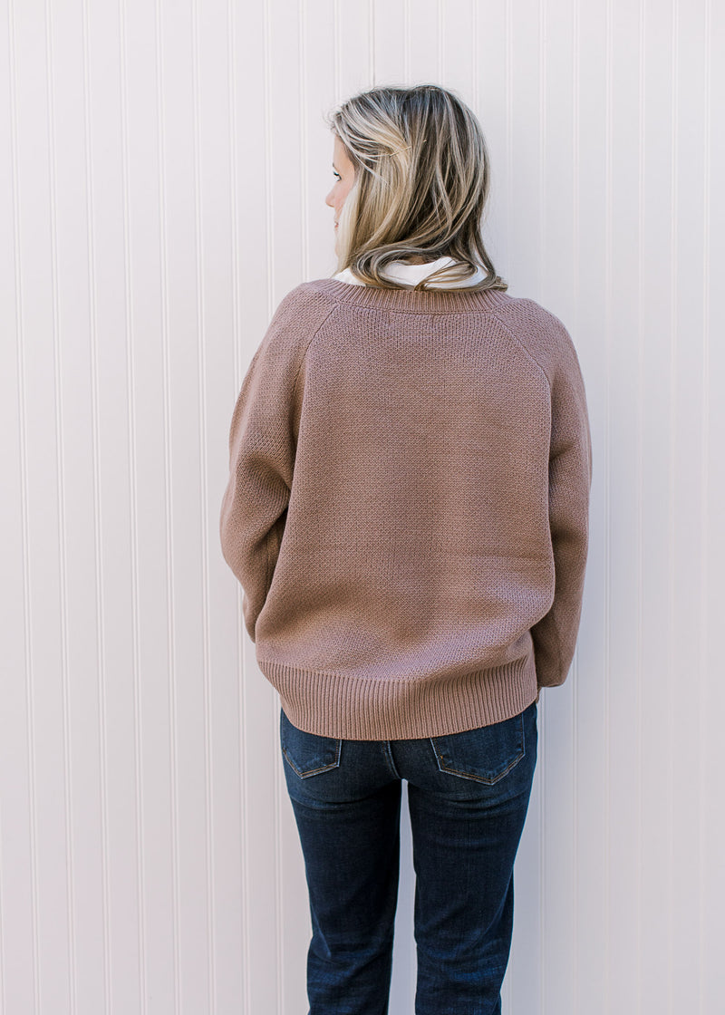 Back view of Model wearing a lavender sweater with white floral bouquet on the front. 