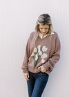 Model wearing jeans with a lavender v-neck sweater with white floral bouquet on the front.