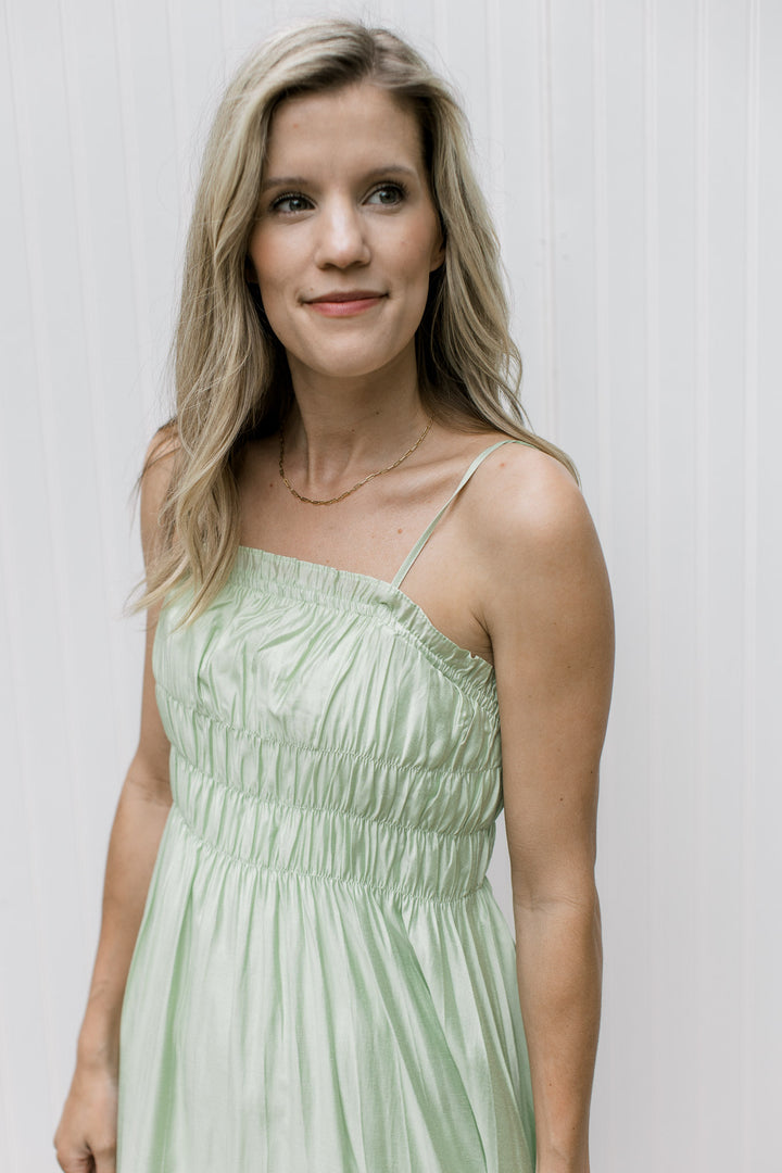 Close up of a smocked bust and pleating detail on a pale green flowy midi. 